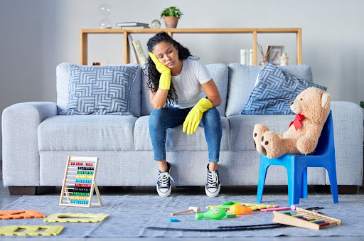 Exhausted caregiver sitting on couch surrounded by children's toys showing signs of parental burnout